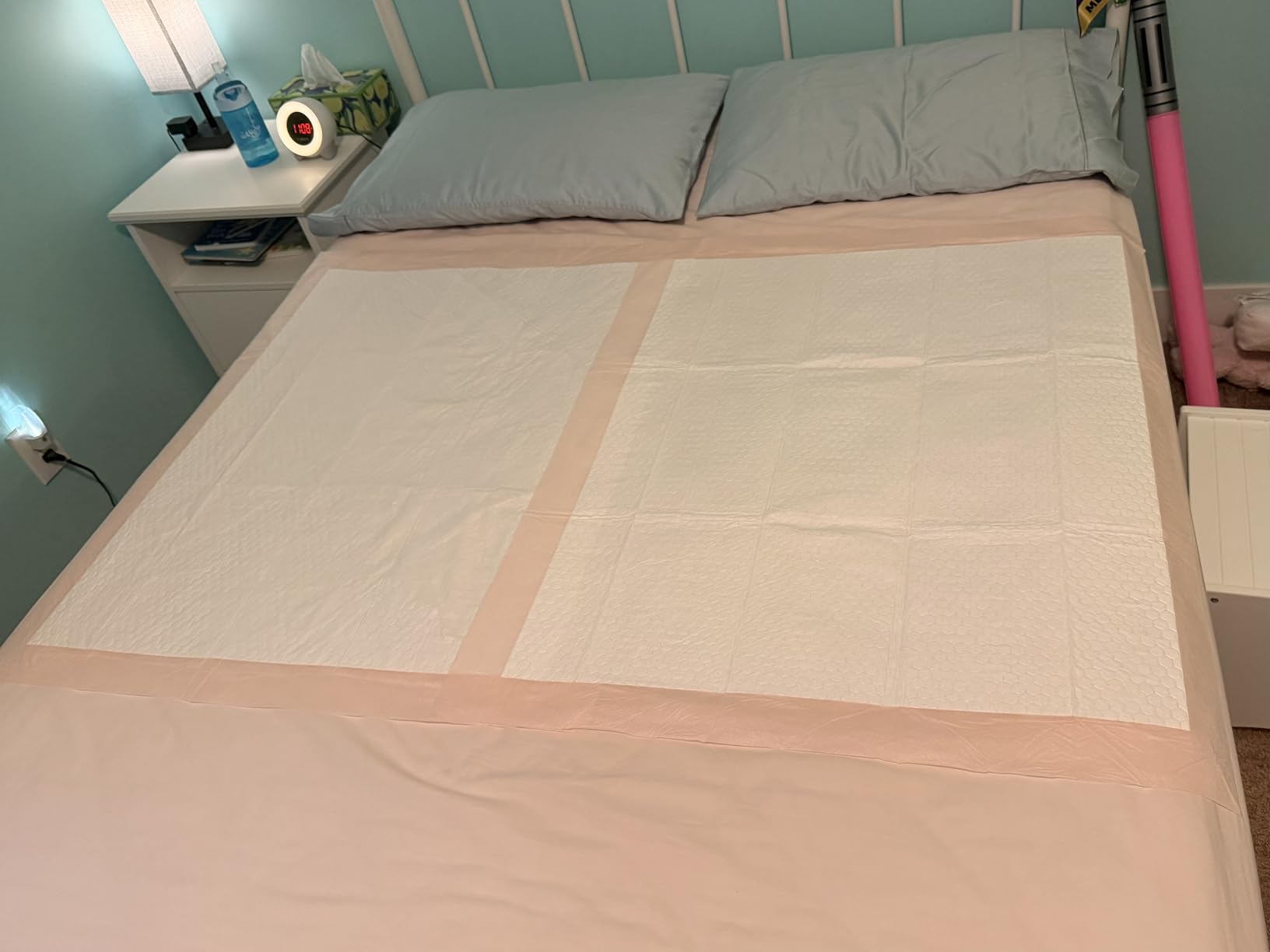 Two peach backed bed pads laid side by side across the middle of a double bed, covering the full width from edge to edge