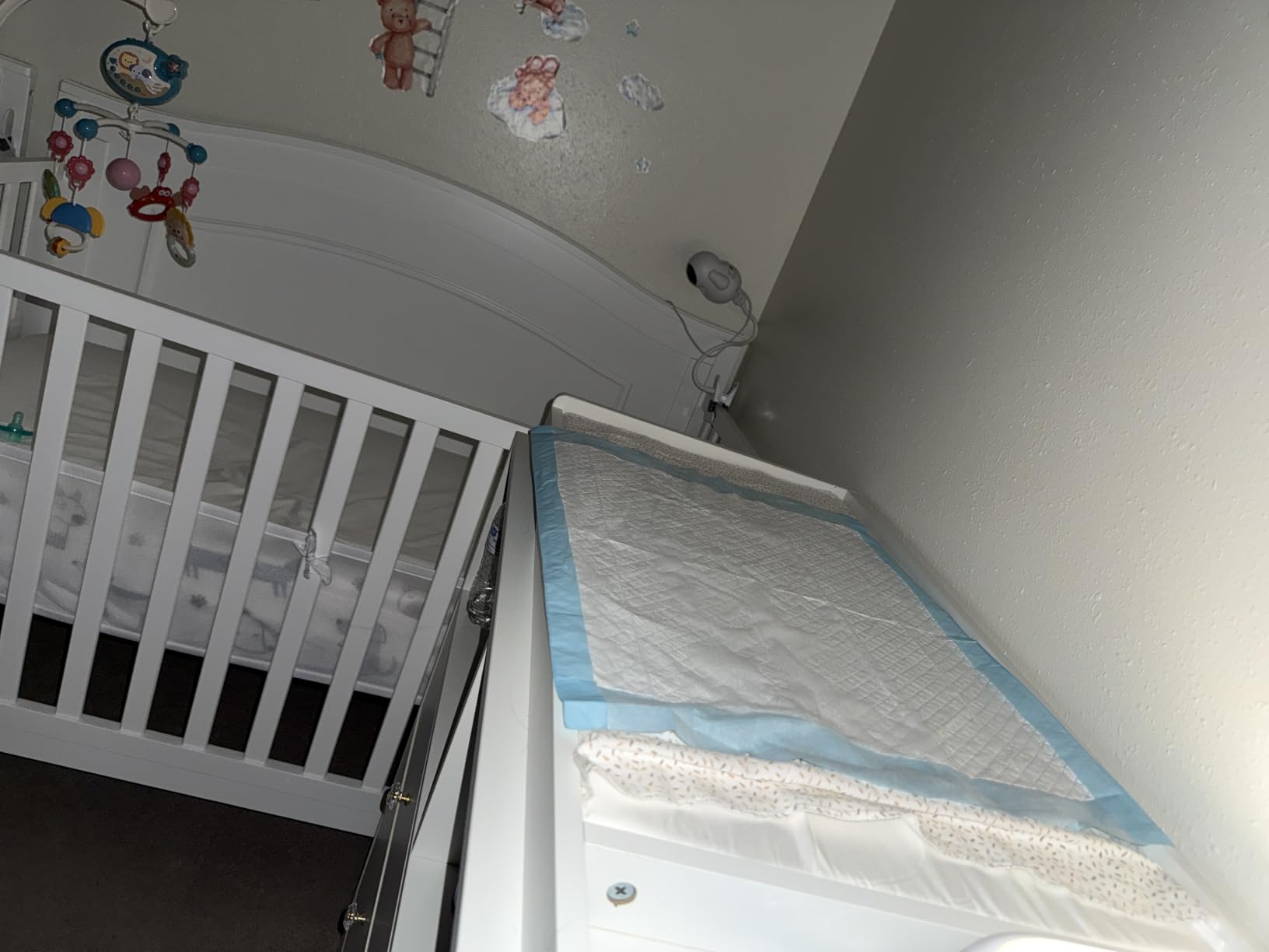 Blue backed disposable underpad laid over a changing table beside a crib in a nursery